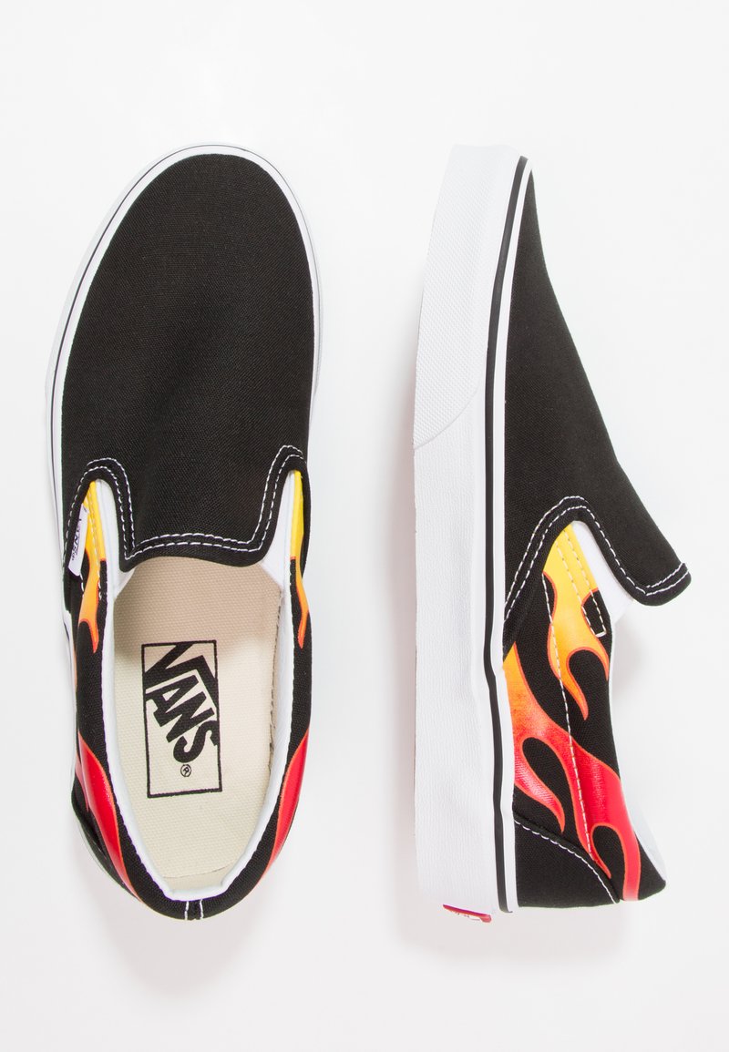 Zapatillas de lona negras sin cordones con un patrón de llamas en rojo, amarillo y naranja; suela de goma blanca y costuras en contraste. Logo de Vans visible en el interior.