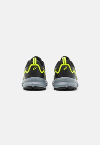Zwarte sportschoenen met gele accenten, voorzien van een textuur bovenkant, een gevoerde kraag en een grijze zool met rubberen noppen voor grip.