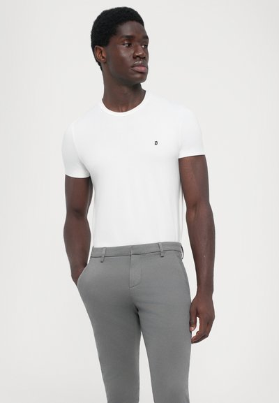 T-shirt bianca a maniche corte con un piccolo logo nero sul petto, abbinata a pantaloni grigi slim-fit. Tessuto liscio con taglio classico.