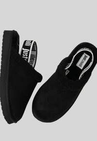 Zoccoli neri slip-on con esterno in morbida pelle scamosciata, interno peloso e suola in gomma texturizzata. Decorati con una fascia con marchio.