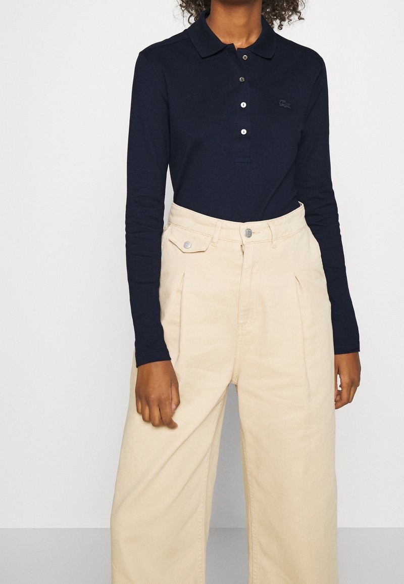 Navy long-sleeve polo shirt with buttons, paired with light beige wide-leg trousers featuring front pleats and metal hardware accents.