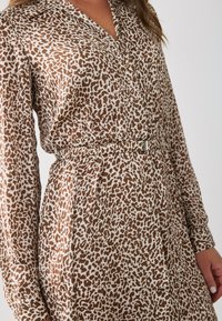 Robe à imprimé léopard marron et blanc avec un col et des manches longues, mettant en avant une taille cintrée avec un accent métallique.
