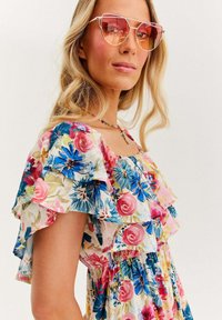 Kwiatowa sukienka z falbaniastymi rękawami w pastelowych kolorach, ozdobiona różowymi i niebieskimi kwiatami. Akcesoria to duże różowe okulary przeciwsłoneczne i kolorowa naszyjnik.