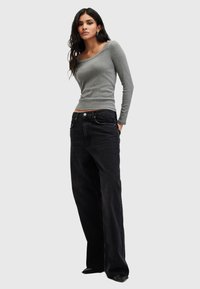 Camicia grigia a maniche lunghe con scollo ampio abbinata a jeans neri larghi. Design semplice, texture liscia e senza motivi o accenti visibili.
