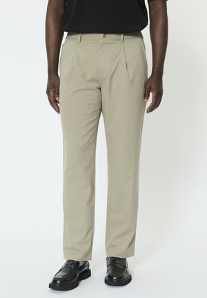 Kaki bukser med et lige ben design, der har forreste læg, knaplukning og lommer. Kombineret med sorte sko.