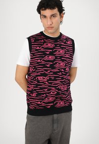 Mouwloze trui in zwart breiwerk met een levendig roze golvend patroon. Witte onderhemd zichtbaar eronder. Casual stijl met geribbelde halslijn.