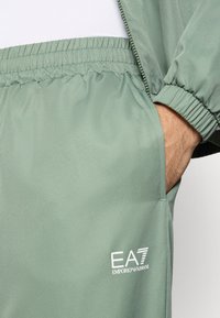 Ανοιχτό πράσινο παντελόνι φόρμας από υφασμάτινη ύφανση, με ελαστ ική μέση και λογότυπο στην εμπρόσθια αριστερή πλευρά.