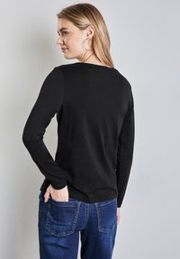 Musta pitkähiainen paita rentoa istuvuutta, yhdistettynä sinisiin denim-farkkuihin. Suuri kangas, pyöreä kaula-aukko ja minimalistinen muotoilu.