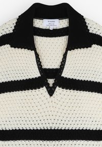 Pull en tricot à rayures noir et blanc avec un décolleté en V et un col à bords festonnés, présentant un design en tricot texturé et ajouré.