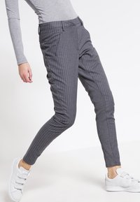 Grijze pinstripe broek met een getailleerde pasvorm, voorzien van voorkruimelpockets en een soepele textuur. Gecombineerd met witte sneakers voor contrast.
