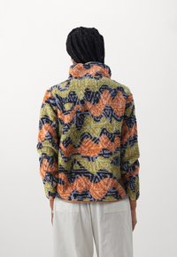 Fleecová mikina s vysokým límcem, texturovaným povrchem a vícebarevným vlnkovým vzorem v odstínech oranžové, zelené, modré a černé.