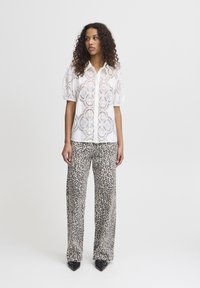 Blouse blanche à motifs en dentelle avec des manches bouffantes, associée à un pantalon large à imprimé léopard. Des chaussures noires à bout pointu complètent l'ensemble.