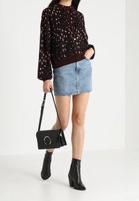 Bordeaux gekleed hoodie met een stippenpatroon, lichtblauwe denim minirok, zwarte enkellaarsjes met hak en een zwarte handtas met een ronde accent.