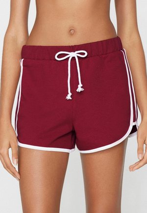 Nahaufnahme einer Person, die bordeauxrote Sportshorts mit weißem Besatz und einem weißen Tunnelzug hat, der in einer Schleife in der Taille gebunden ist.