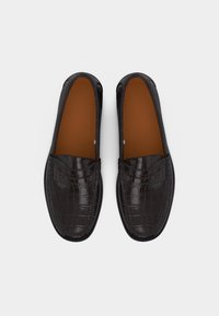 Ζευγάρι μαύρα δερμάτινα loafers με μοτίβο κροκό, καφέ εσωτερικές σόλες, φωτογραφημένα από πάνω σε λευκό φόντο.