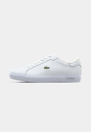 White leather sneaker with a smooth surface, green crocodile logo, white lace-up closure, padded collar, and clear rubber sole.