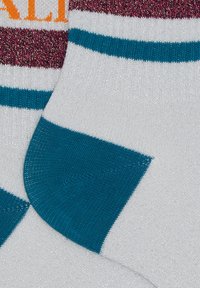 Bunt gestreifte Socken mit weißem Stoff und silbernen Glitzerpartikeln, teal- und burgunderfarbenen Streifen und kräftigem orangem Text.