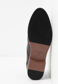 Semelle d'une chaussure de ville en cuir marron texturé avec une semelle en caoutchouc noir, étiquetée « ANNA FIELD 37 », présentée sur fond blanc.