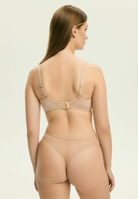 Beżowy biustonosz z regulowanymi ramiączkami i zapięciem na haftkę, w komplecie z pasującą cielistą bielizną. Gładka faktura i minimalistyczny design.