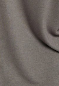 Tissu lisse de couleur brun clair avec de doux plis et une texture fine, créant des ombres et des reflets délicats.