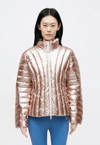 Rózsaarany színű, nagykosaras kabát magas gallérral, steppelt mintával és cipzáras záródással. Fényes felülettel és oldalzsebekkel rendelkezik.