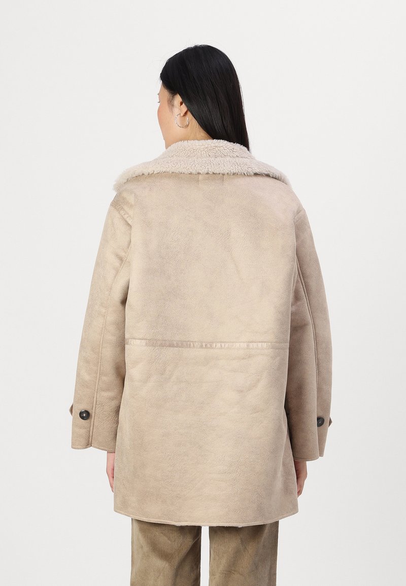 Manteau beige doublé en shearling avec une surface texturée, grand col et poignets boutonnés, présentant un design à coupe droite et un détail de couture au dos.