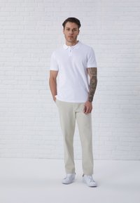 White polo shirt with short sleeves, paired with light beige trousers and white sneakers. Smooth texture, casual design.