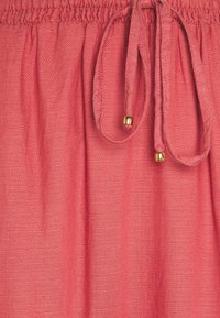Tessuto leggero color corallo con una finitura testurizzata; presenta una vita elastica e un cordoncino con perline decorative dorate.