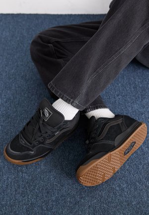 Baskets noires en daim et en textile, avec une semelle en gomme, un col rembourré, des coutures blanches et un patch logo sur la languette.