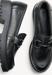 Černé kožené mokasíny s kulatou špičkou, nízkým podpatkem, dekorativní sponou a texturovanou podrážkou. Povrch je hladký s jemnými švy.