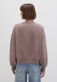 Cotton pullover sweater in muted mauve, featuring a ribbed texture, dropped shoulders, and a cropped fit, paired with light blue denim.