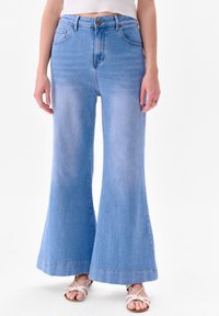 Uitlopende lichtblauwe denim jeans met een hoge taille, een knoopsluiting en een grote zoom. Soepele textuur met twee voorkraaien en stikseldetails.