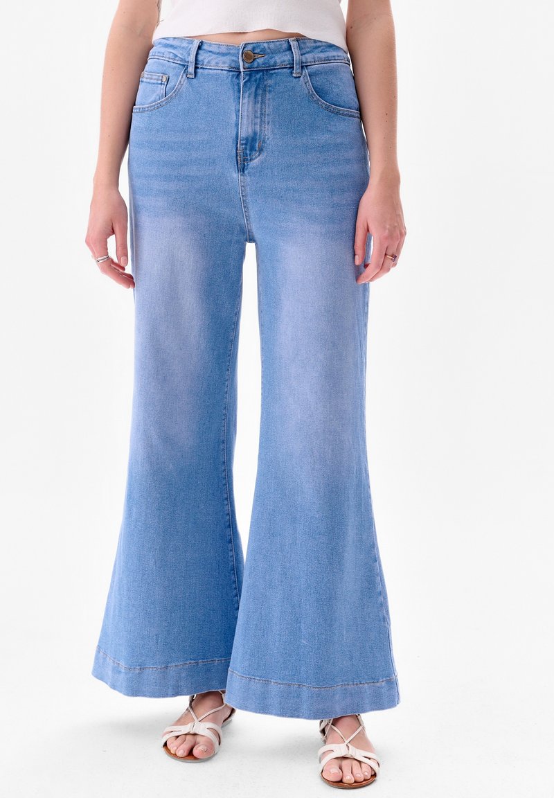 Uitlopende lichtblauwe denim jeans met een hoge taille, een knoopsluiting en een grote zoom. Soepele textuur met twee voorkraaien en stikseldetails.