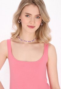 Top rosa senza maniche con scollatura quadrata. La modella indossa una collana di perline viola con piccoli dettagli floreali e orecchini a cerchio viola abbinate.