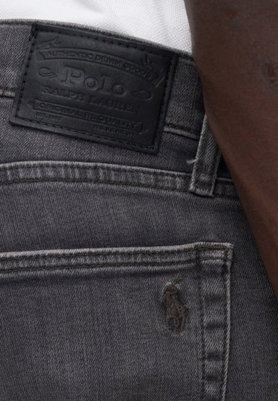 Os jeans de ganga cinza apresentam um patch em pele preta com uma marca em relevo na parte de trás, com costura contrastante e detalhes de design minimalistas.
