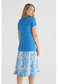 Korte-mouwen blauwe top gecombineerd met een luchtige blauw-witte rok met een patroon en een gerimpelde zoom, wat een casual, gelaagd outfitontwerp laat zien.