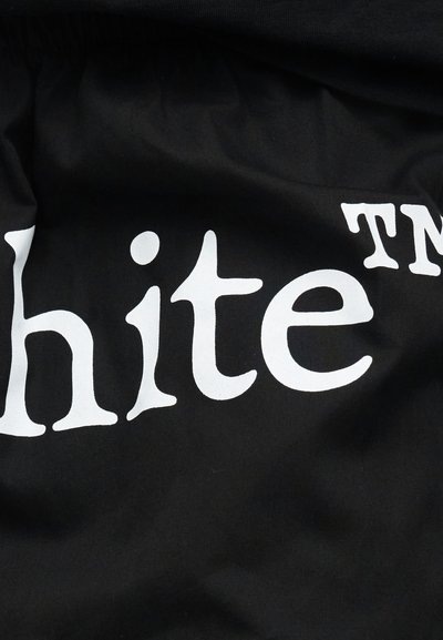 Texte stylisé blanc épelant « hite » avec un symbole de marque déposée sur un fond de tissu noir froissé.