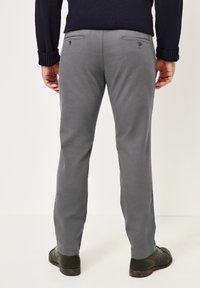 Graue Freizeithosen mit geradem Schnitt, zwei Gesäßtaschen und einer glatten Stoffoberfläche. Kombiniert mit schwarzen Schuhen und einem dunklen Pullover.