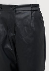 Pantalons en cuir noir avec une texture lisse, taille élastique et une poche latérale. Comprend une fermeture à bouton, un design ajusté et un détail de pli.