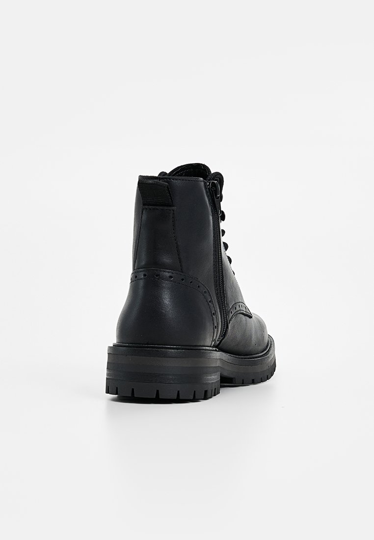 Schwarze Lederknöchelstiefel mit Schnürverschluss, seitlichem Reißverschluss, strukturiertem Obermaterial und robuster Gummisohle. Brogue-Verzierung entlang des Schafts.