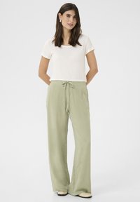 Ľahké, bledozelené ľanové nohavice s pásom na šnurovanie, skombinované s priliehavým bielym bavlneným tričkom a plochými béžovými topánkami.