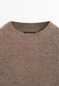 Brązowy prążkowany sweter z okrągłym dekoltem. Tkanina ma teksturowany wzór i drobne plamki, z metką z napisem "Massimo Dutti".