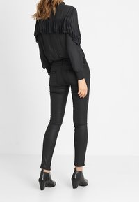 Blusa negra plisada con detalles de volantes, combinada con pantalones ajustados negros de aspecto cuero y botas negras hasta el tobillo. Diseño sencillo con texturas suaves.