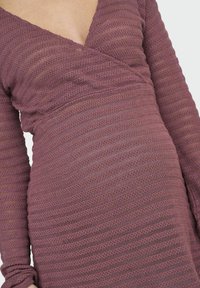 Ilga rankovė suknelė turtingos mauve spalvos, su tekstūruota, dryžuota rašte, giliais V formos iškirpimu ir susiraukšlėjimu juosmens srityje.