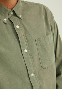 Camicia in corda verde oliva con colletto button-down, tasca anteriore e bottoni perla, che mette in mostra una trama a righe verticali.