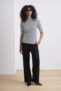 Zwart-wit gestreepte top met korte mouwen en gekartelde randen, gecombineerd met zwarte wijde pantalons en pumps met scherpe neuzen.