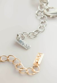 Silver and gold layered chain bracelets featuring oval links, rectangular tags with raised lettering, and a shiny finish.