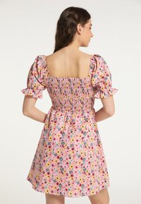 Rochie cu imprimeu floral din material roz, având mâneci bufante, decolteu pătrat și detalii cu elastic la spate. Formă în A, cu o lungime scurtă.