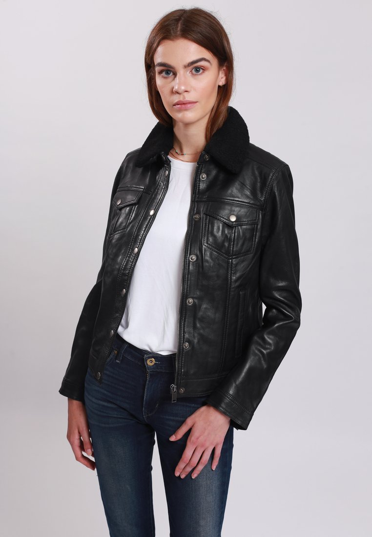 Schwarze Lederjacke mit einem Kunstfellkragen, mit Vordertaschen und einem Reißverschluss ausgestattet. Über einem weißen Oberteil getragen und mit blauen Jeans kombiniert.