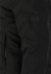 Svart puffjacka med texturerat tyg, diagonalt kviltad design och en cirkulär logotyp med texten "Whistler" på övre ärmen.
